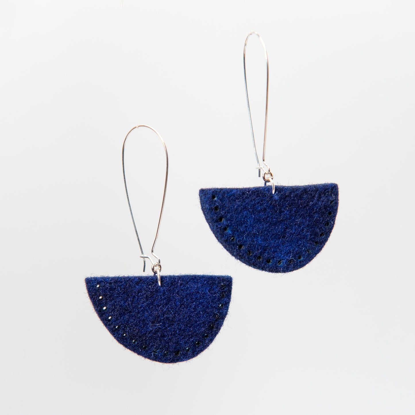 Two dark blue semi-circular earrings with small dark accents hang from silver hooks.