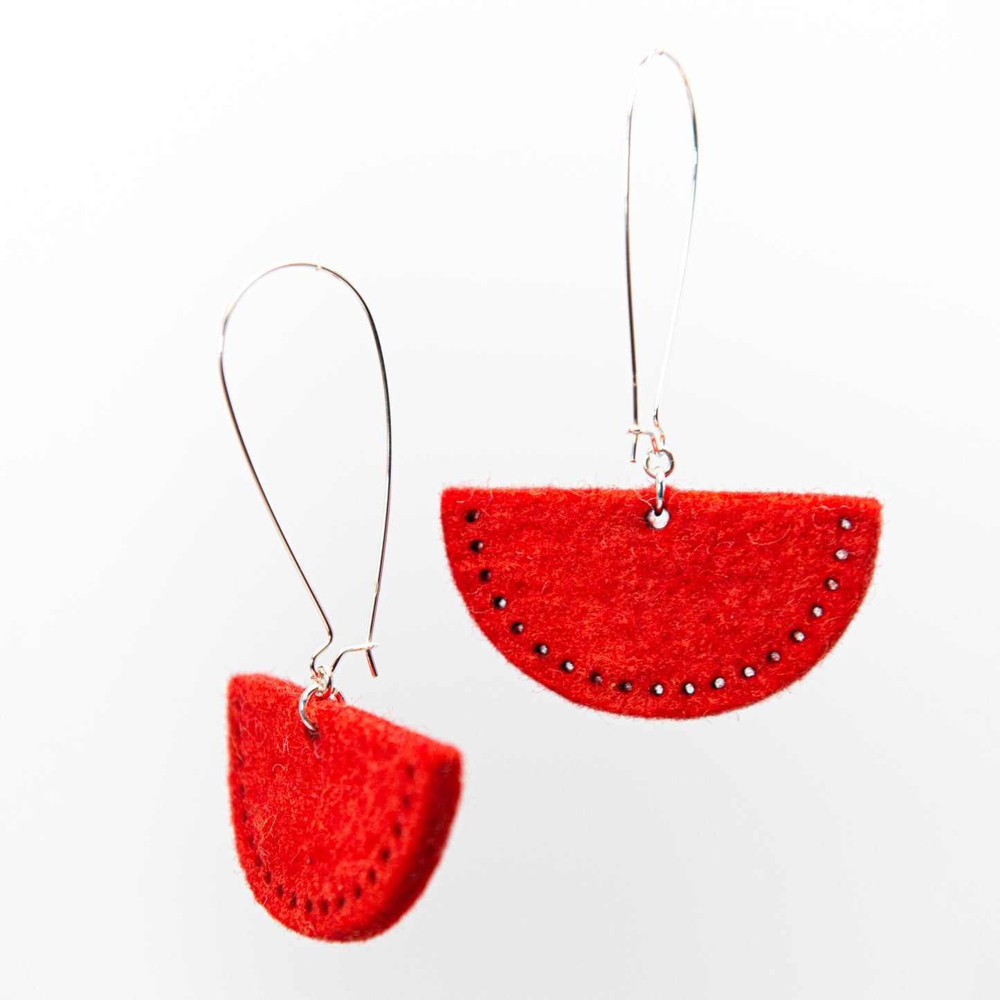Two red semi-circular earrings with small dark accents hang from silver hooks.
