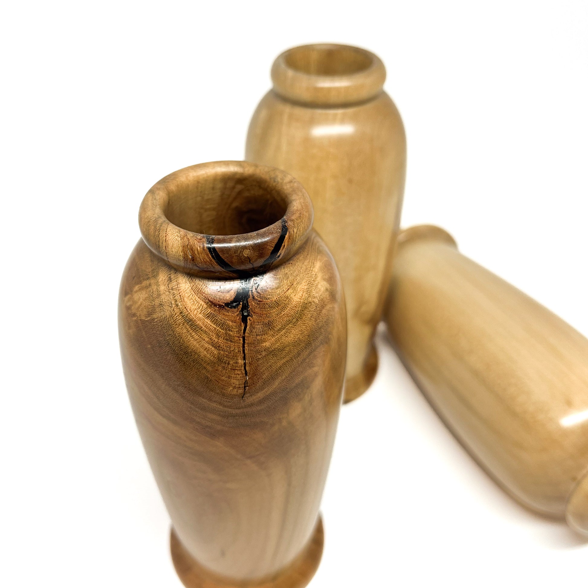 Close-up angled view of three small, polished wooden vases with natural wood grain and rounded openings.