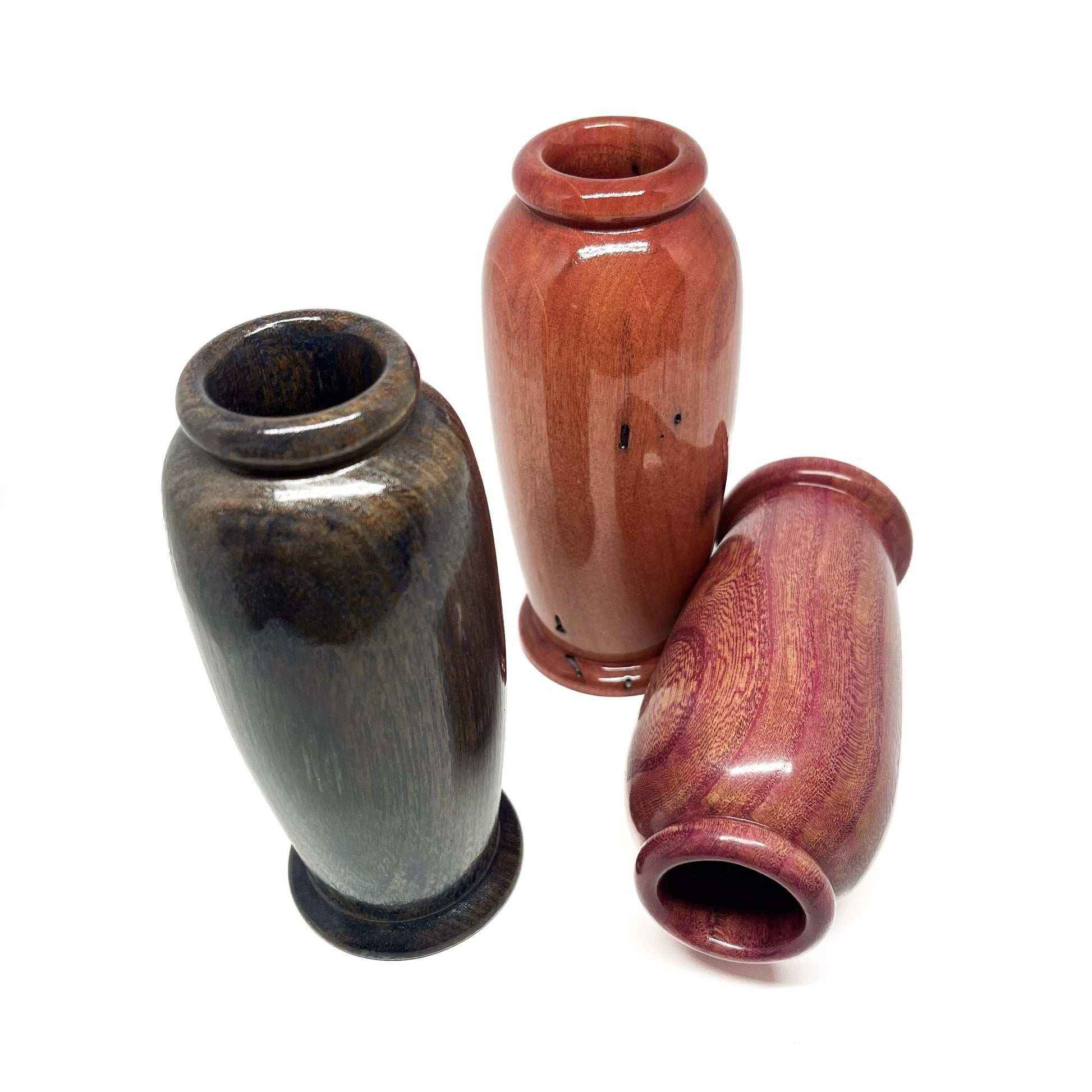Overhead angled view of three small, polished wooden vases with distinct wood tones and rounded openings.