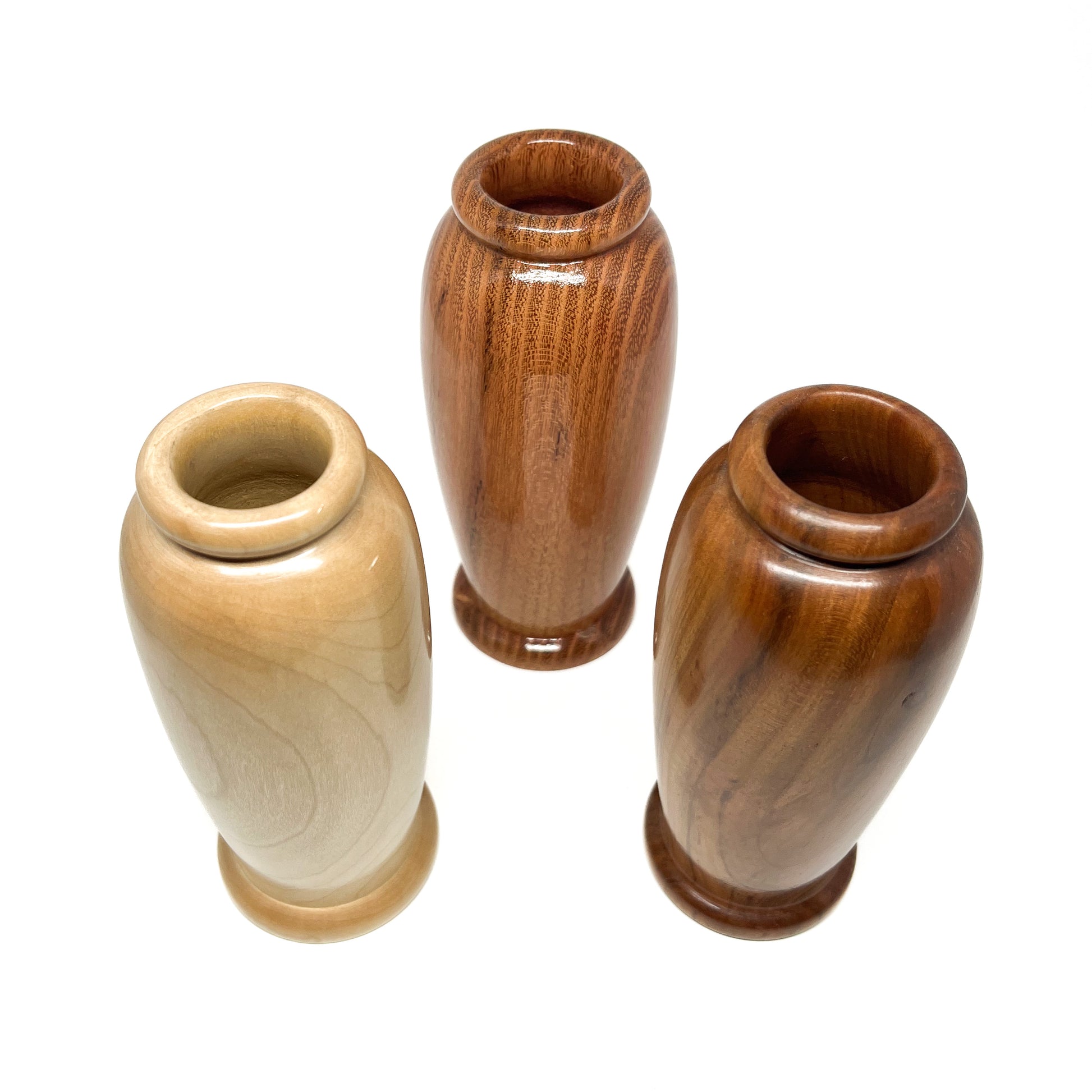 Overhead view of three small, polished woodturning vases with varying wood tones and rounded openings.