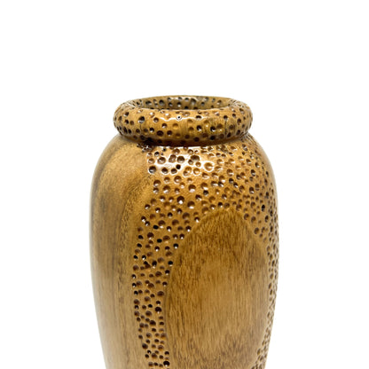 Close-up of a small, textured wood vase with carved circular patterns and small perforations around the opening.
