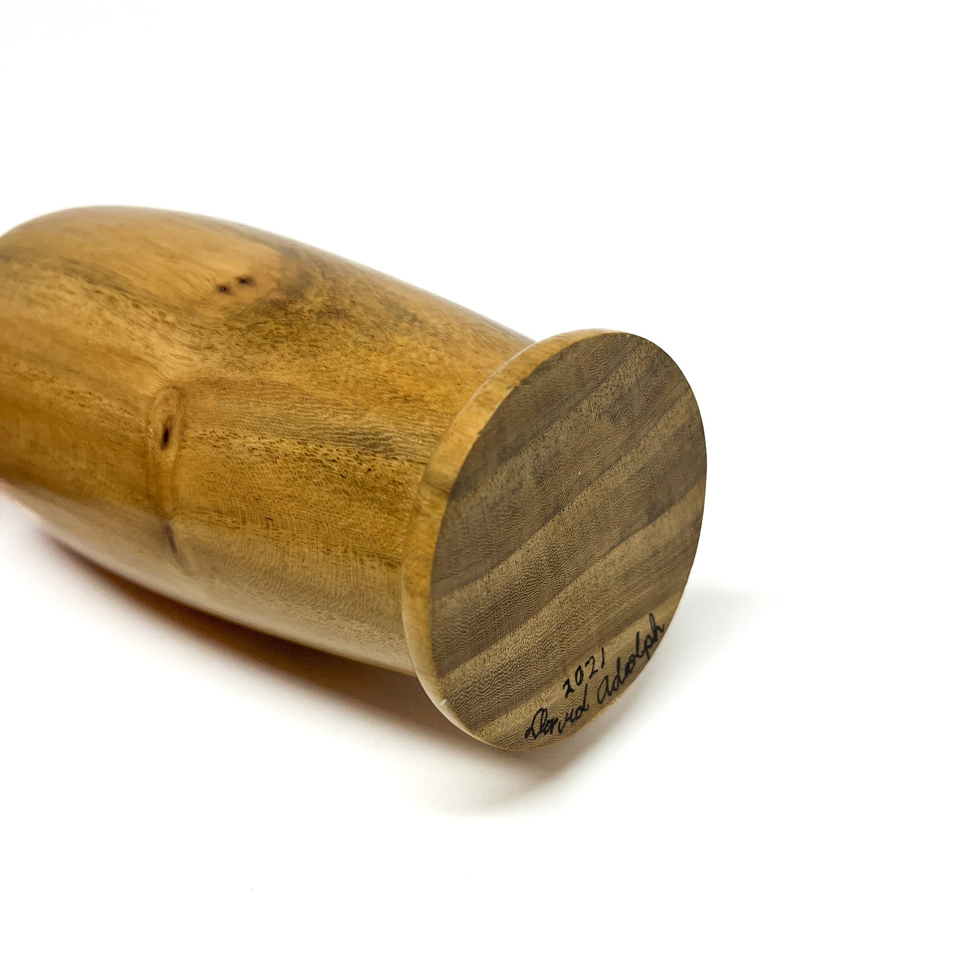 Angled view of a smooth wooden vase lying horizontally, showing the base with a signature and "2021".