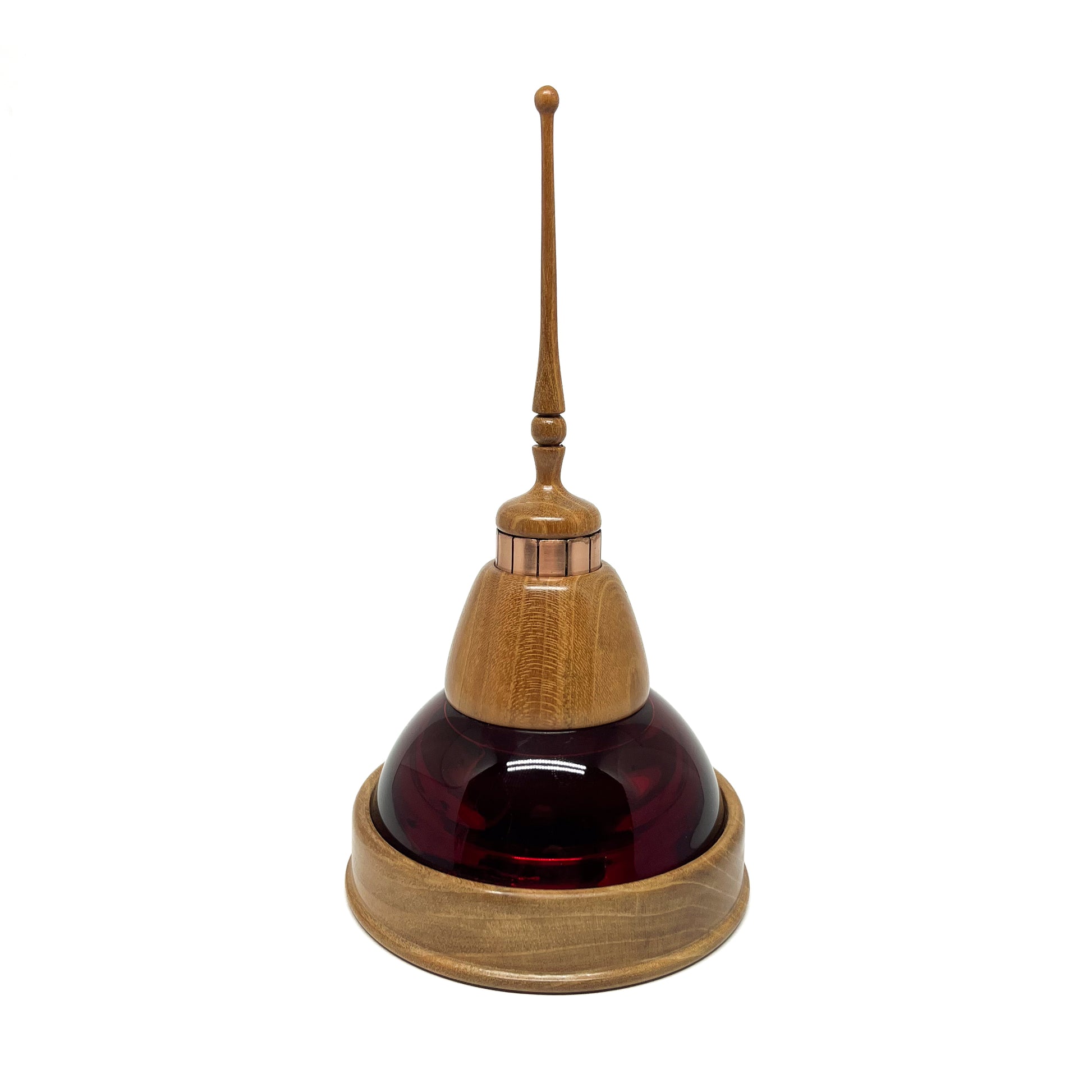 Mixed media sculpture with a dark red glass dome, wooden base and top, copper accents, and a slender wooden spire.