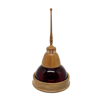 Mixed media sculpture with a dark red glass dome, wooden base and top, copper accents, and a slender wooden spire.