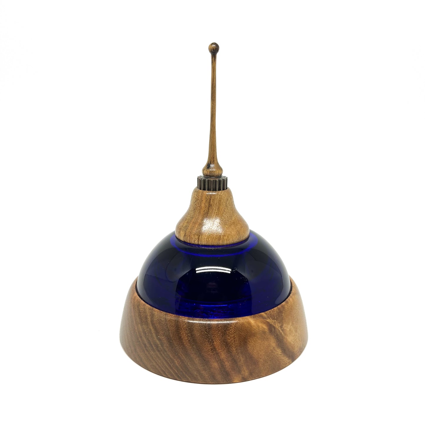 Mixed media sculpture with a deep blue glass dome, layered wooden base and top, metal accents, and a slender wooden spire.