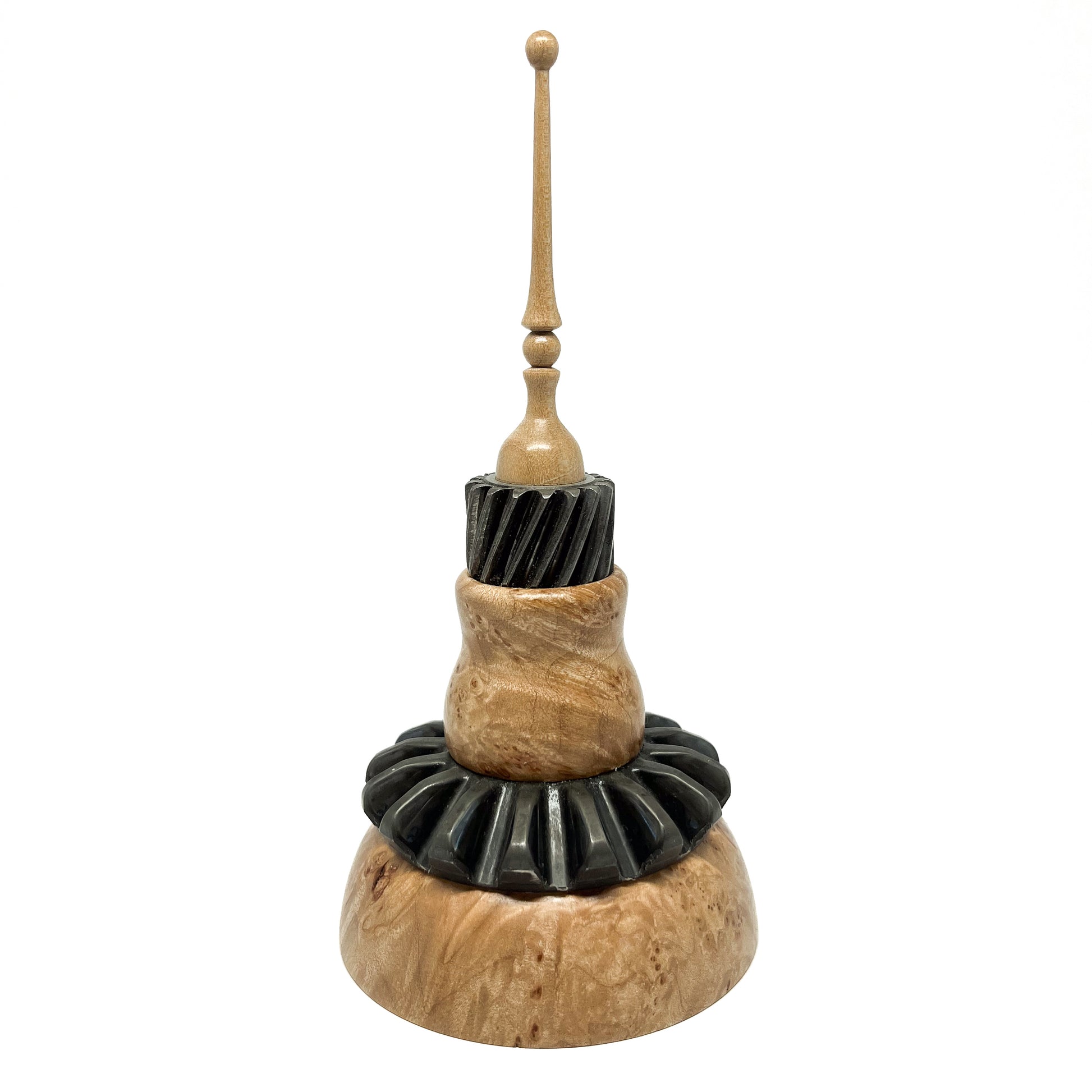 Stacked mixed media spire sculpture with wood, black ridged elements, and a slender, topped spire.