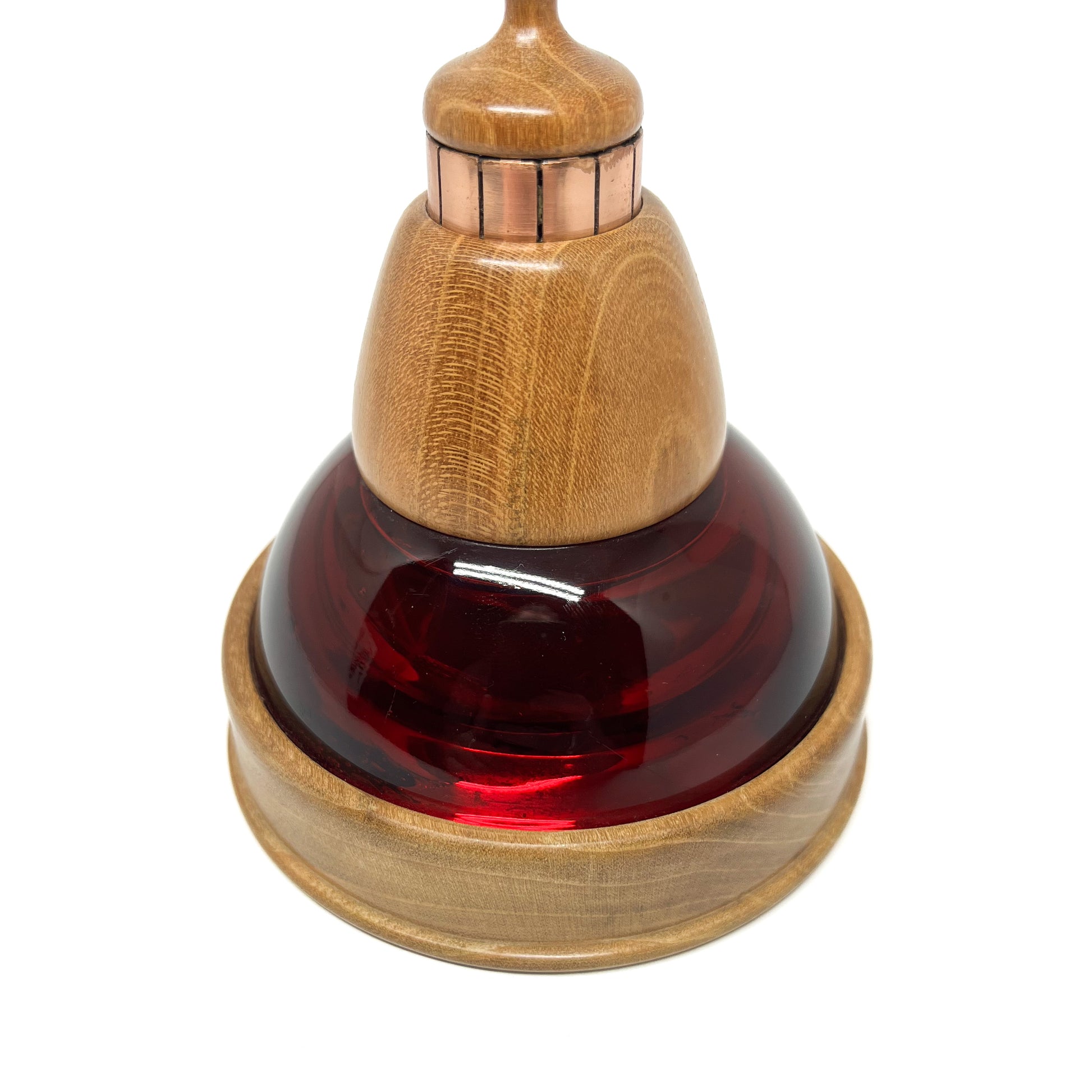 Close-up of a mixed media sculpture with a deep red glass dome, wooden components, and copper vertical strips.