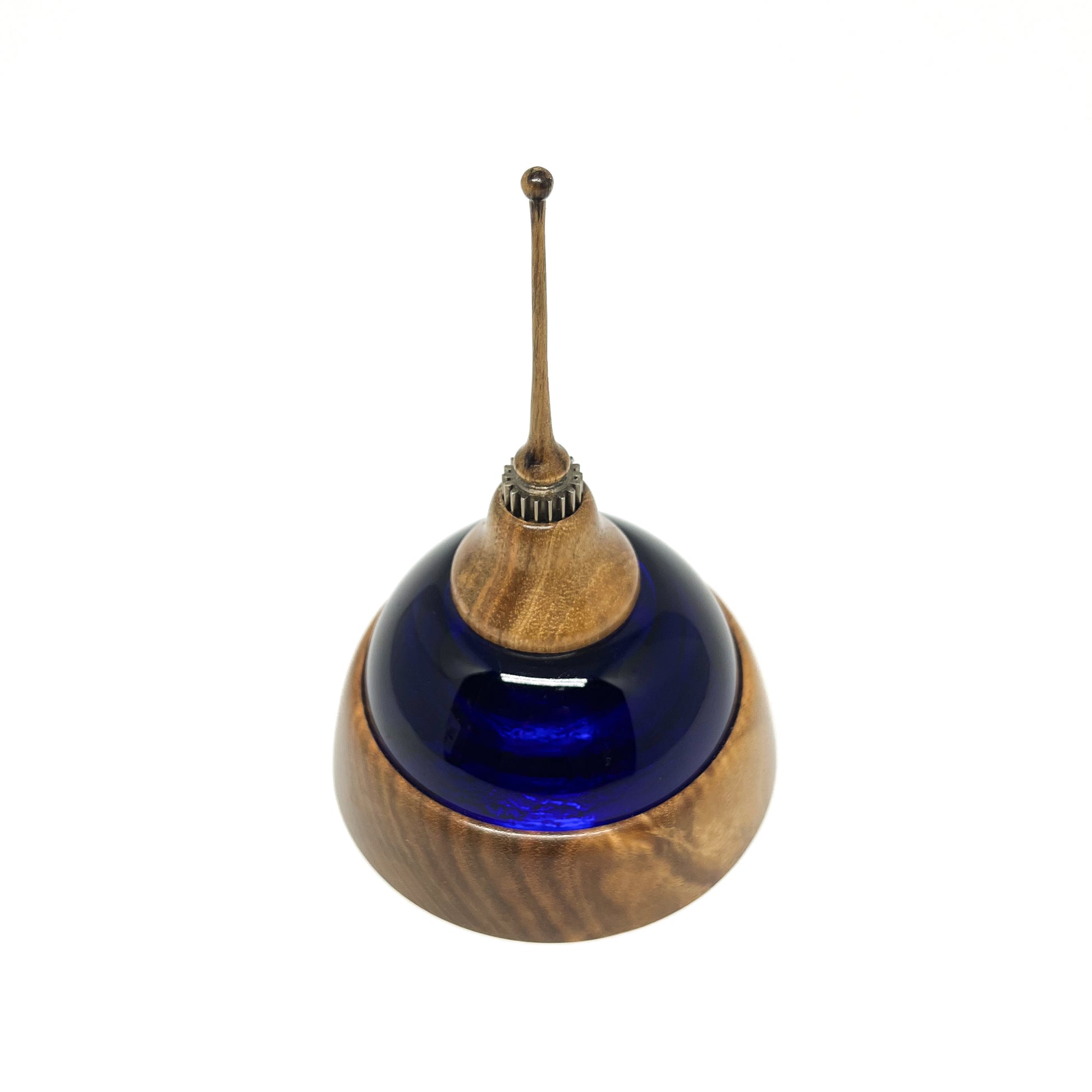 Overhead view of a mixed media sculpture with a deep blue glass dome, wooden base and top, metal details, and a thin spire.