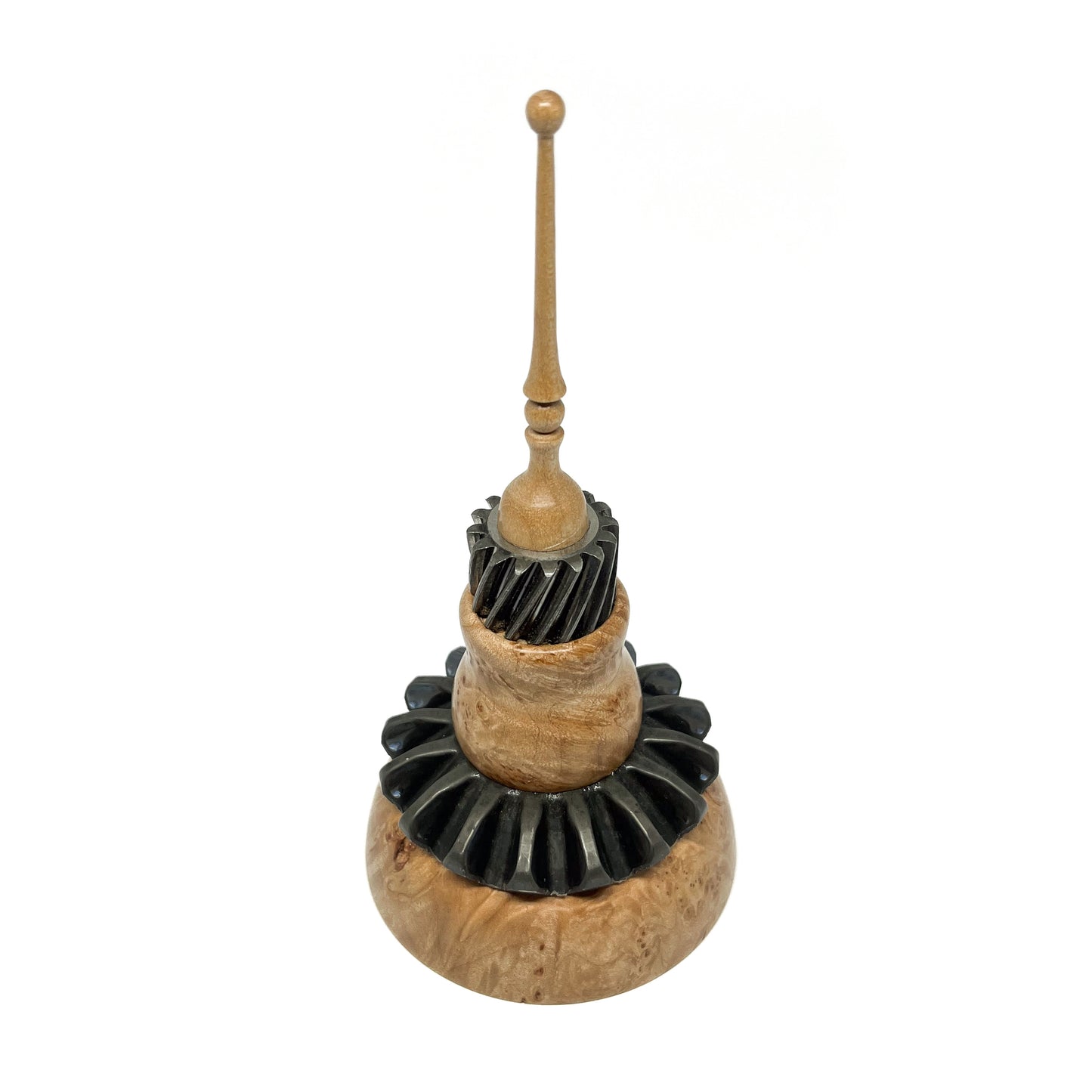 Mixed media spire sculpture with layered wood and black textured elements, topped with a slender wooden spire.