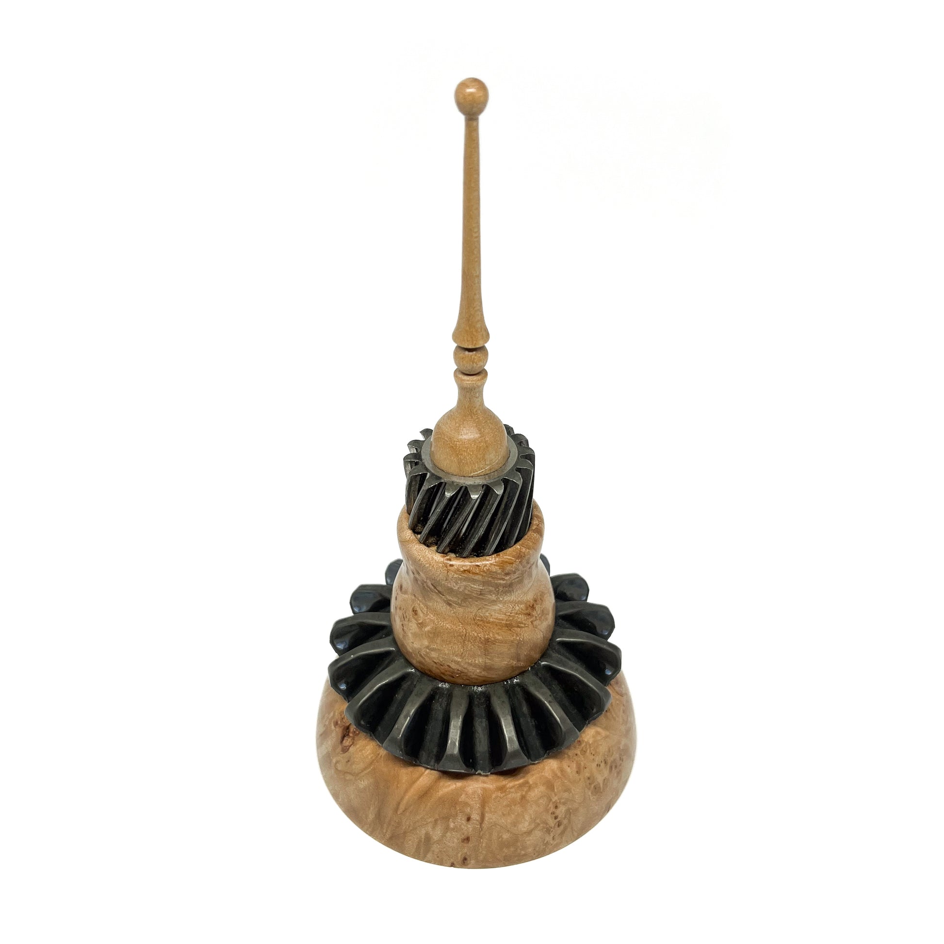 Mixed media spire sculpture with layered wood and black textured elements, topped with a slender wooden spire.