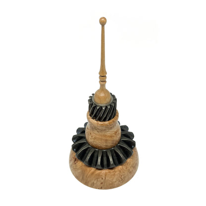 Mixed media spire sculpture with layered wood and black textured elements, topped with a slender wooden spire.
