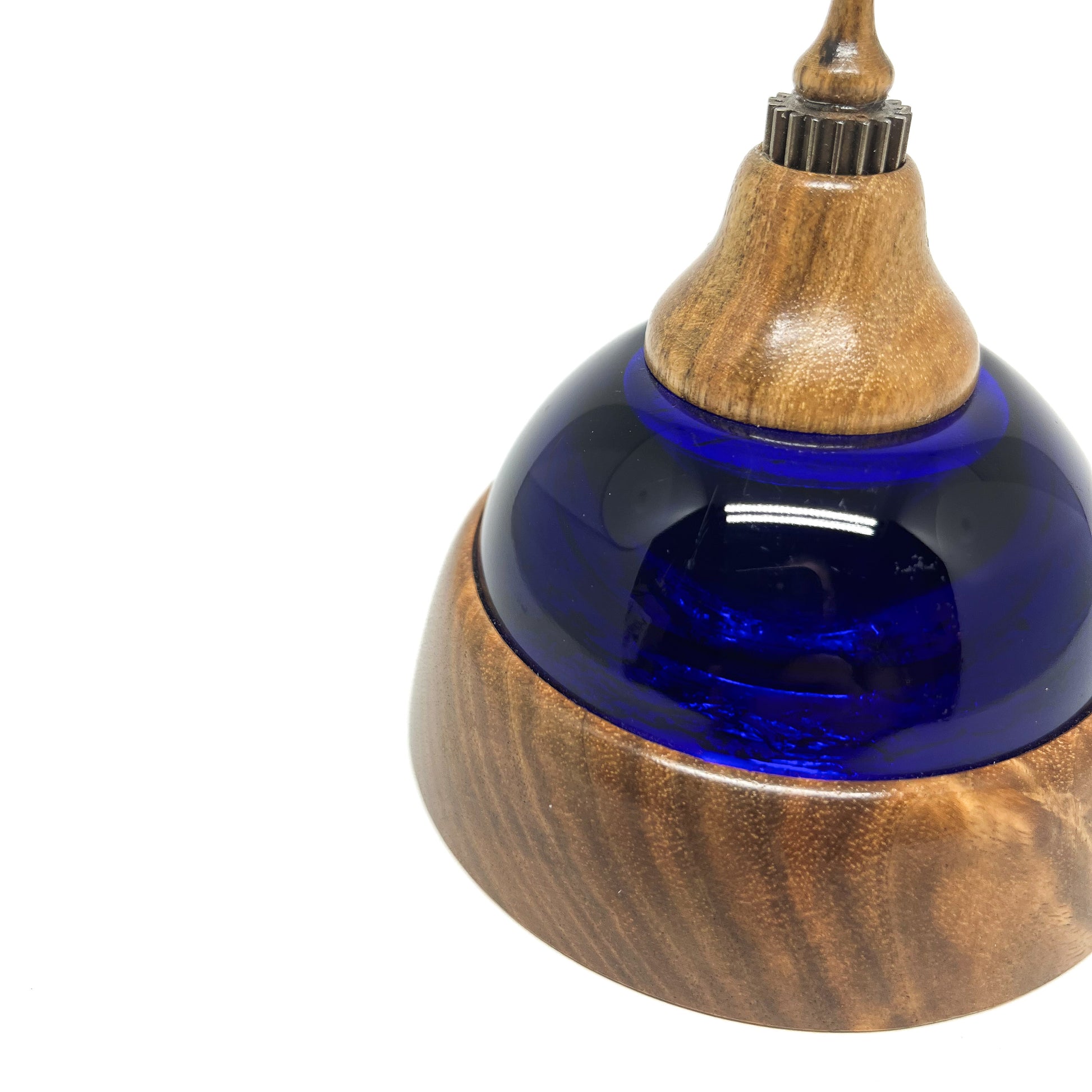 Close-up of a mixed media sculpture with a deep blue glass dome, wooden base and top, and textured metal accents.