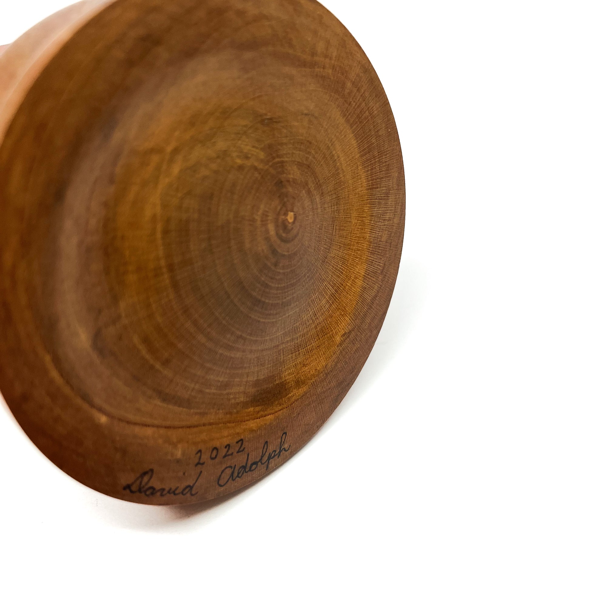 Close-up of the wooden base of a sculpture with concentric rings and a handwritten signature "David Adolph 2022".