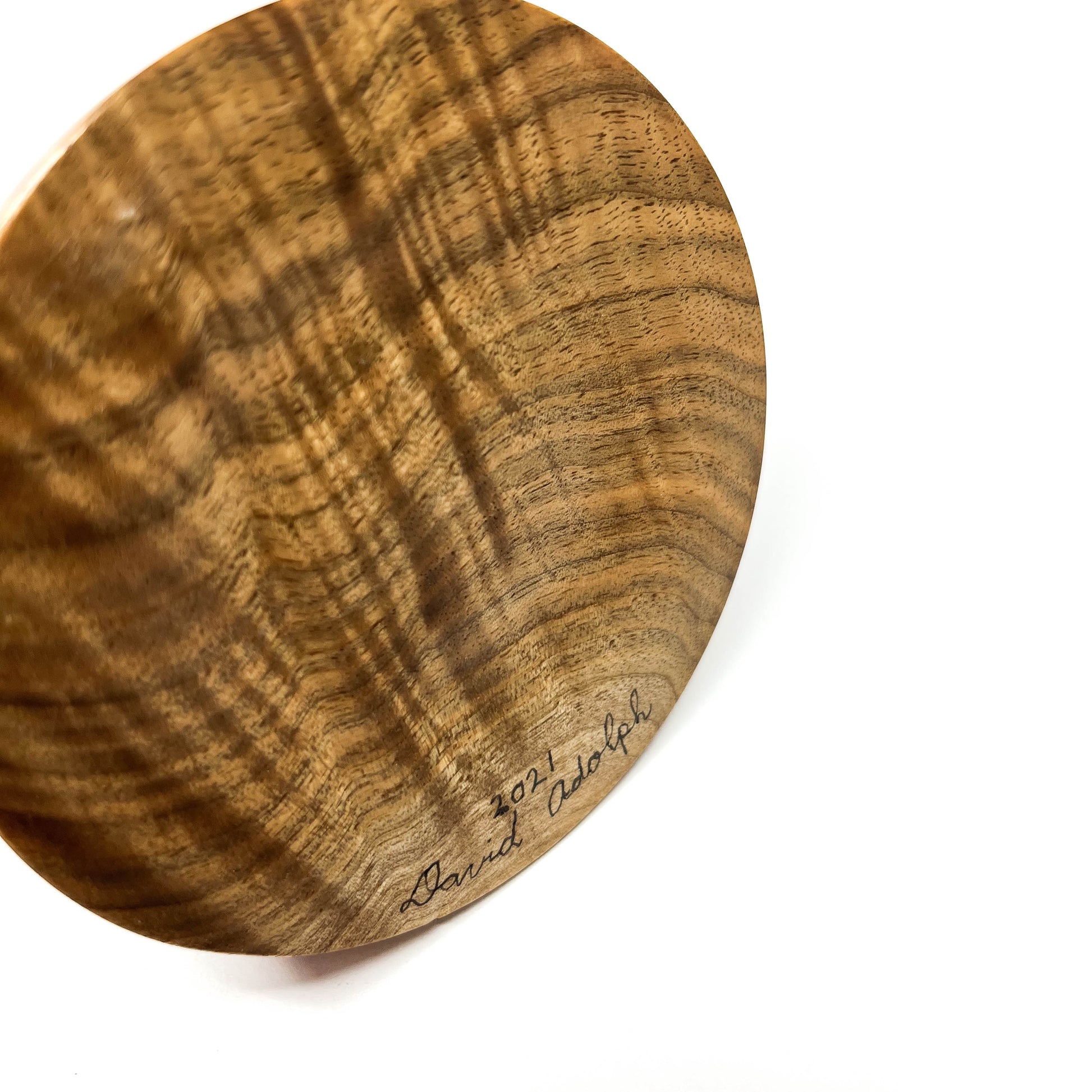 Close-up of the textured wooden base of a sculpture signed "David Adolph 2021".