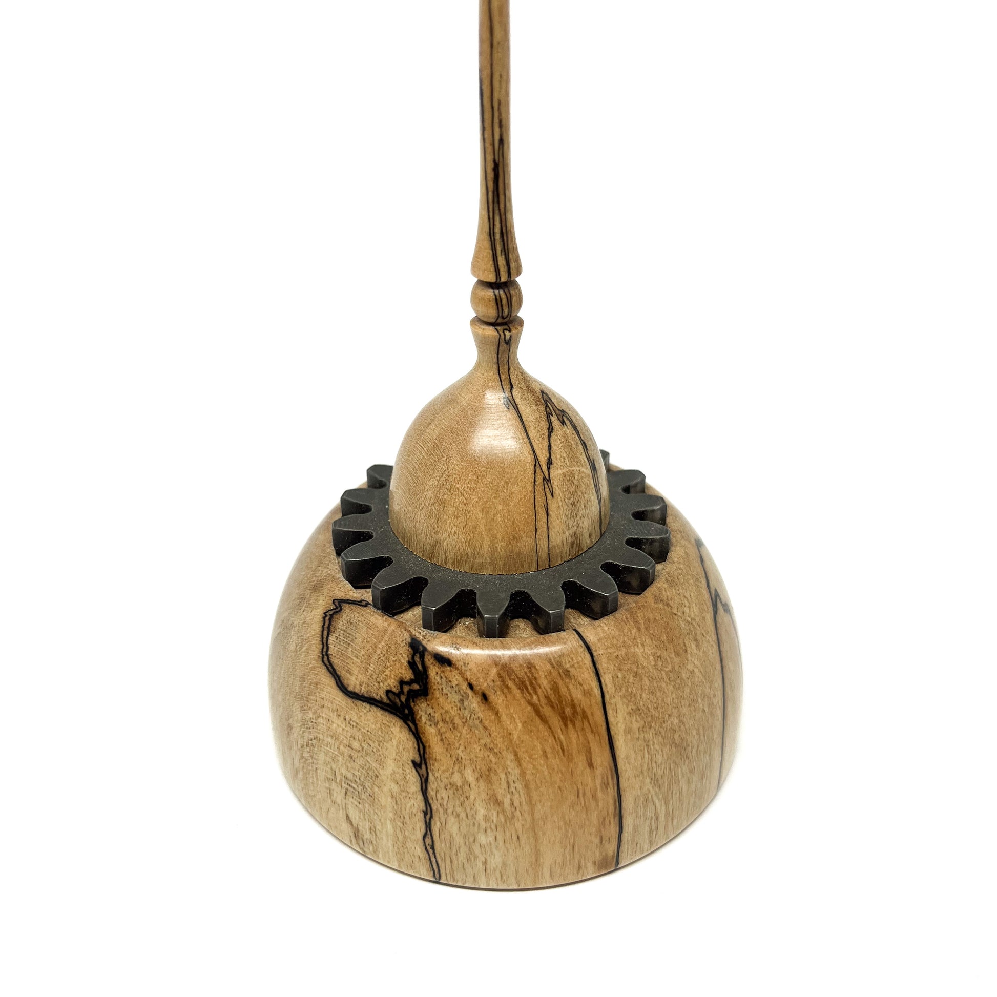 Close-up of a small wood spire sculpture with a dark, cog-like ring and a tall, slender, detailed spire.