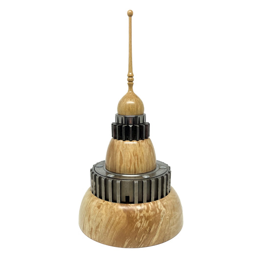 Stacked wood spire sculpture by David Adolph with multiple dark, cog-like rings and a tall, slender, topped spire.