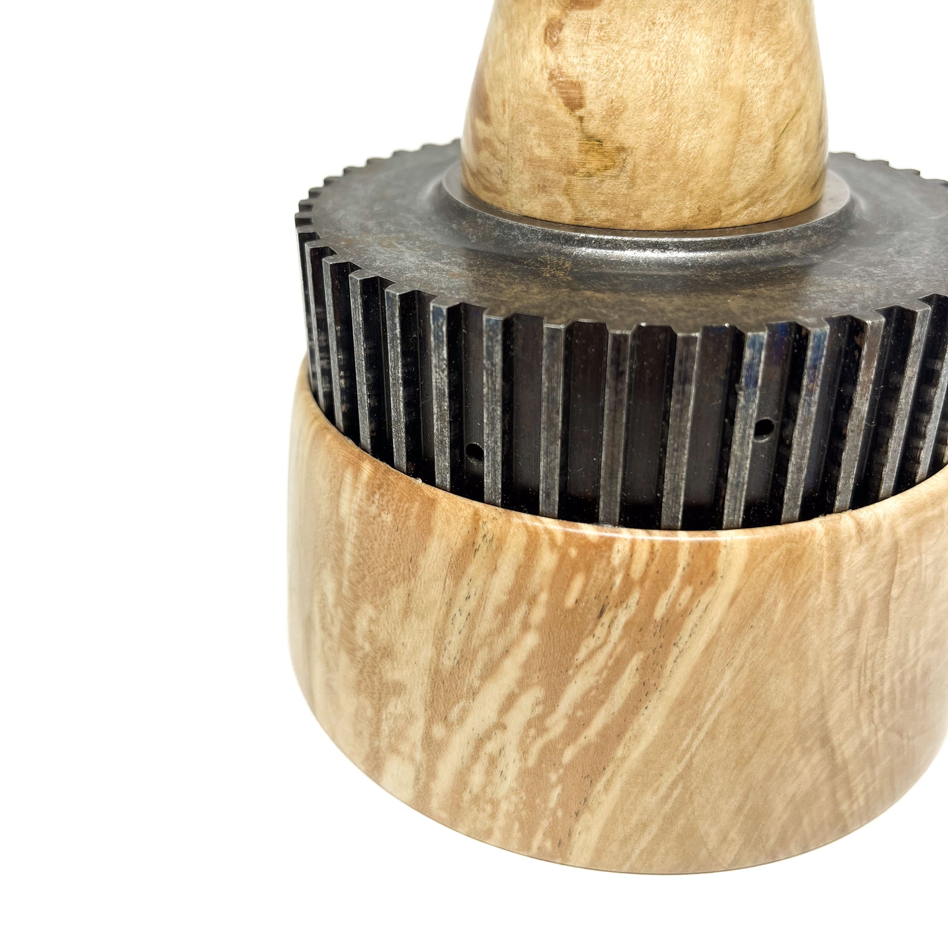 Close-up of the textured wood base and dark, cog-like ring of a spire sculpture.
