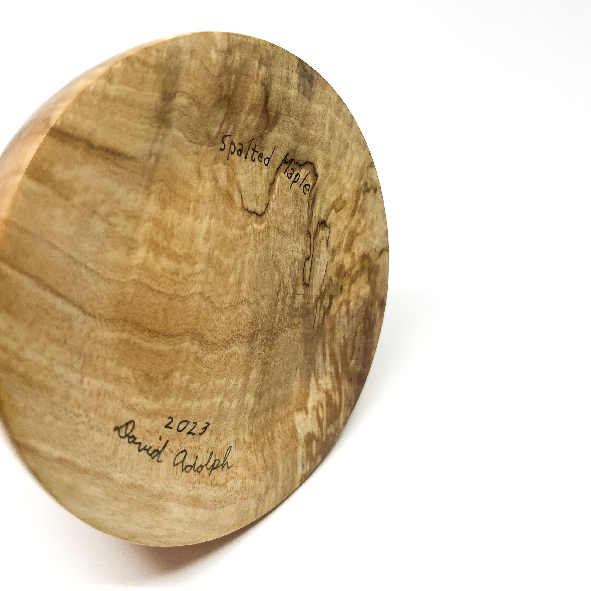 Close-up of the textured wood base of a sculpture signed "Spalted Maple 2023 David Adolph".