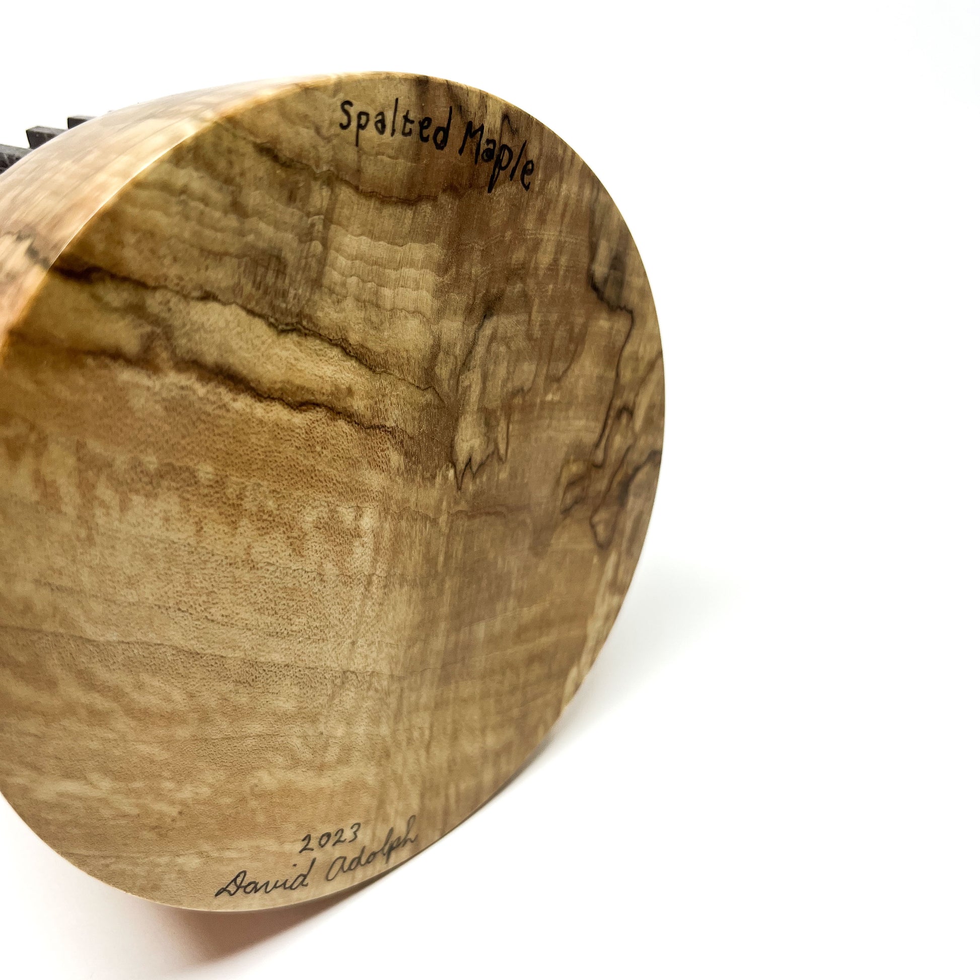 Close-up of the textured wood base of a sculpture signed "Spalted Maple 2023 David Adolph".