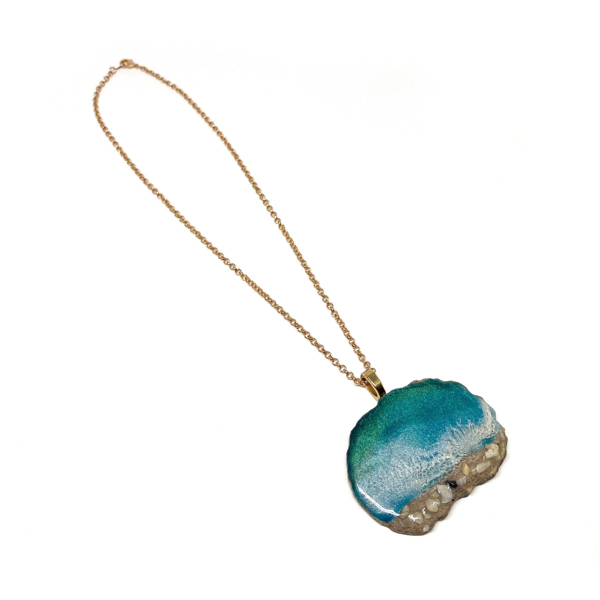 A necklace with an ocean-inspired pendant, featuring blue resin and sand-like textures.