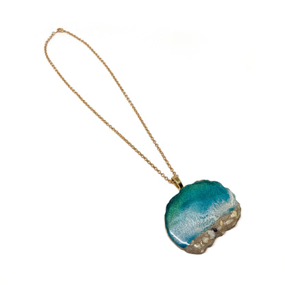 A necklace with an ocean-inspired pendant, featuring blue resin and sand-like textures.