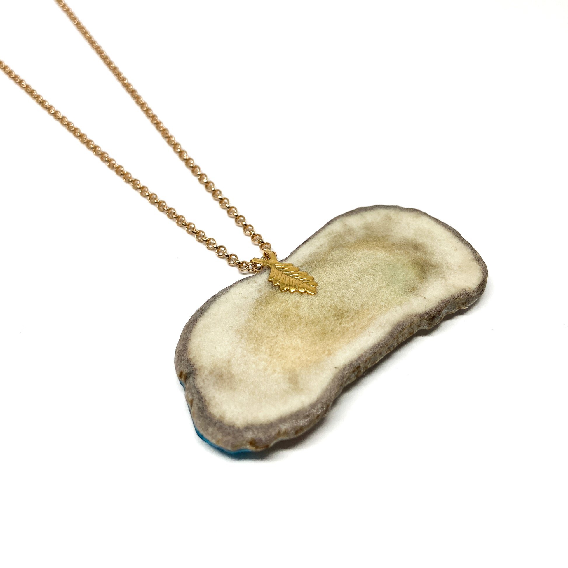 A necklace with a pendant made from a slice of antler, featuring a gold leaf charm and chain.