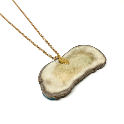 A necklace with a pendant made from a slice of antler, featuring a gold leaf charm and chain.