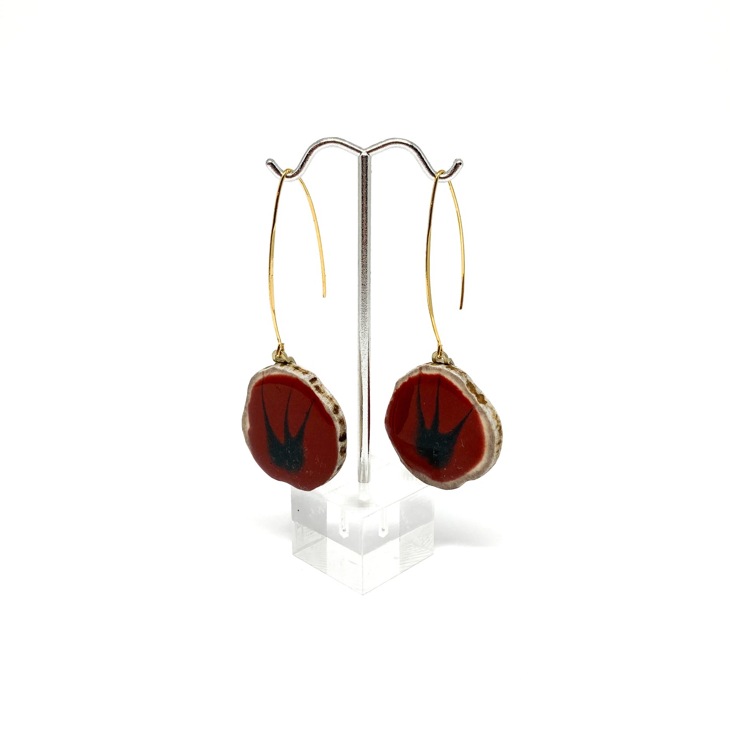 Two round earrings with red and black bird-shaped designs, displayed on a silver earring stand.