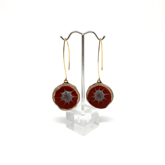 Two round earrings with red and gray starburst patterns, displayed on a silver earring stand.