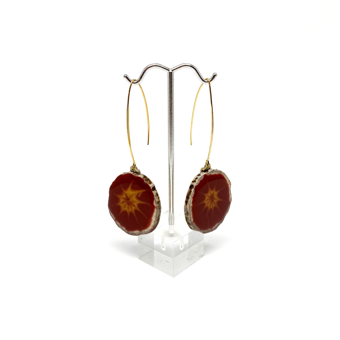 Two round earrings with red and gray starburst patterns, displayed on a silver earring stand.