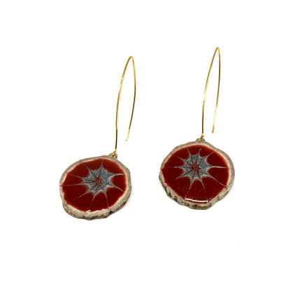 Two round earrings with red and gray starburst patterns, featuring gold hooks.