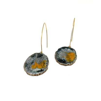 Two round earrings with black, white, and gold abstract designs, featuring gold hooks.