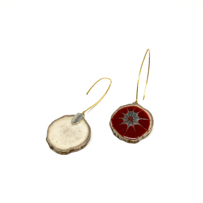 Two mismatched earrings, one with a red and gray starburst pattern, the other with a slice of antler and a gold hook.