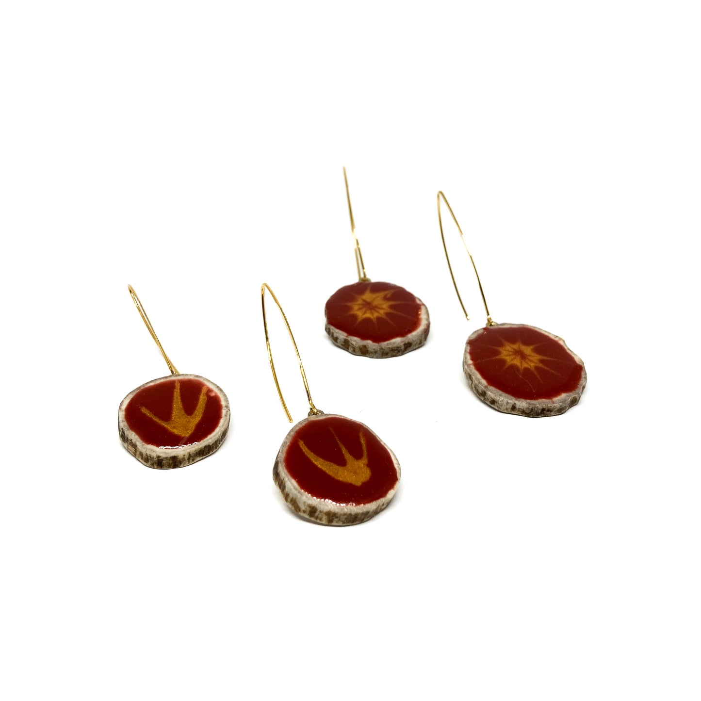 Four round earrings with red and gold designs, featuring gold hooks. Two have bird-shaped designs, two have starburst patterns.