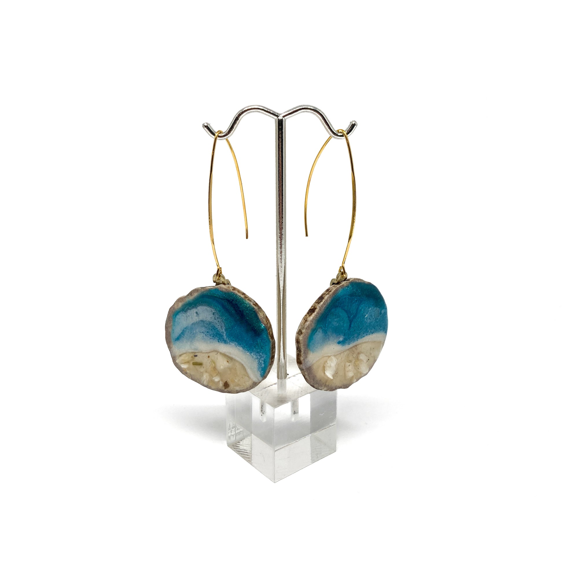 Two round earrings with blue and white geode-like designs, displayed on a silver earring stand.