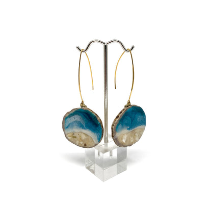 Two round earrings with blue and white geode-like designs, displayed on a silver earring stand.