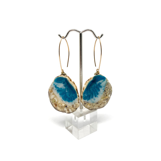 Two round earrings with blue and white geode-like designs, displayed on a silver earring stand.