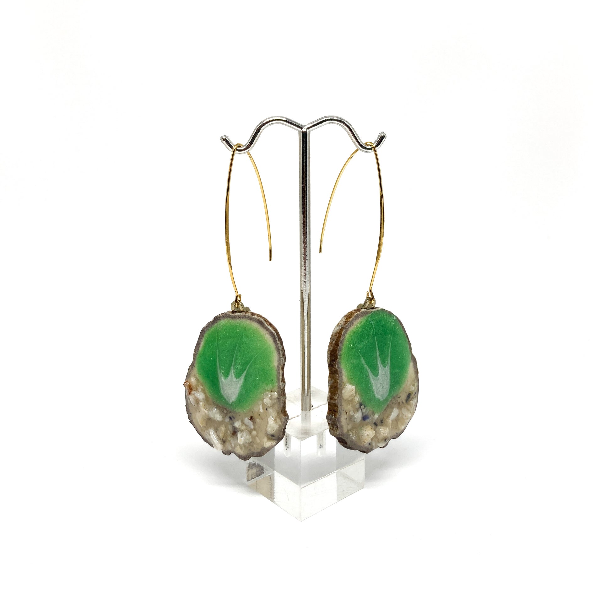 Two round earrings with green and white leaf-shaped designs, displayed on a silver earring stand.