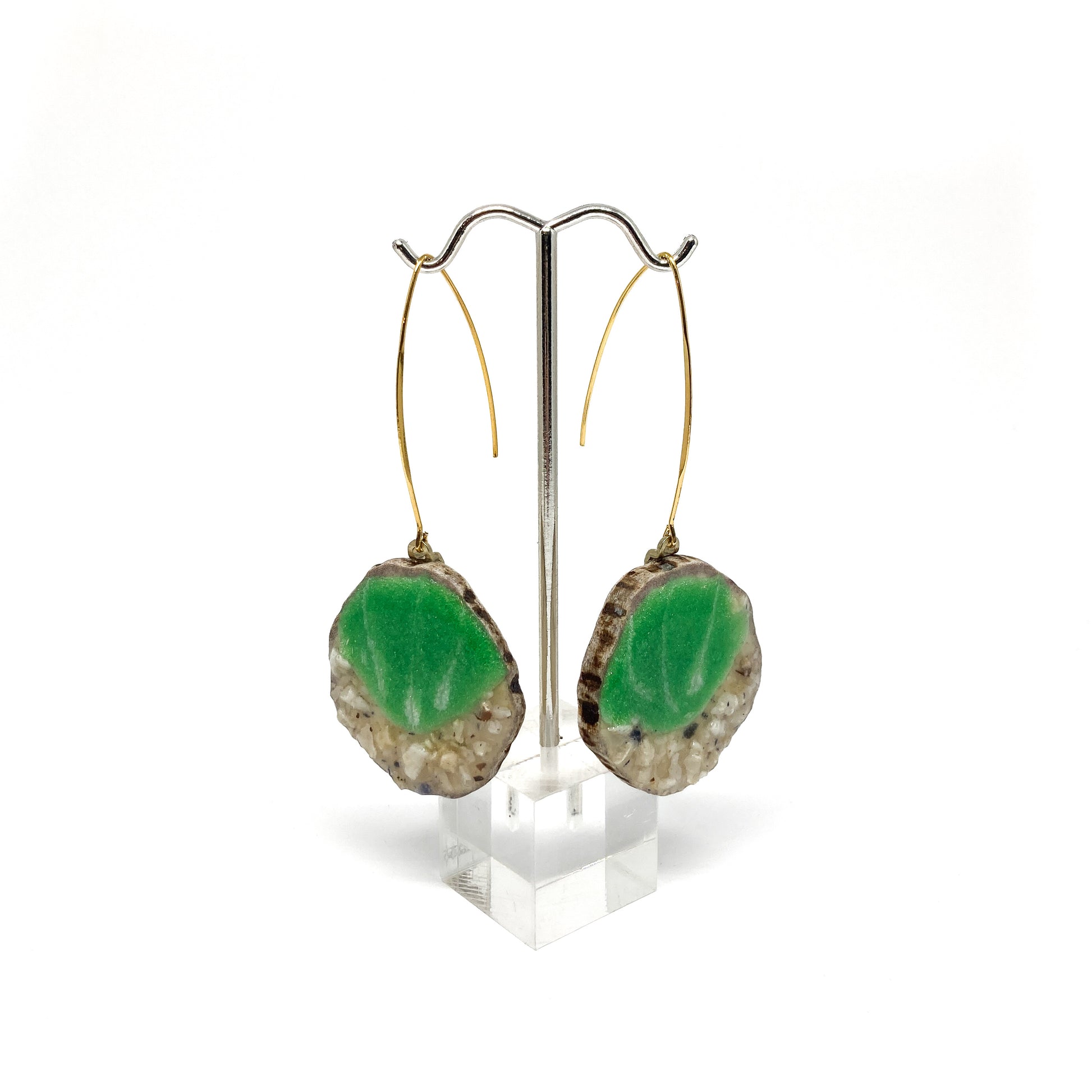 Two round earrings with green and white leaf-shaped designs, displayed on a silver earring stand.