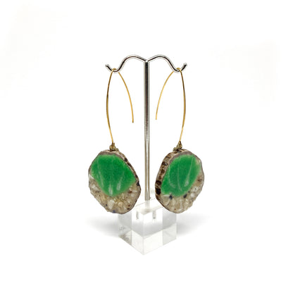Two round earrings with green and white leaf-shaped designs, displayed on a silver earring stand.