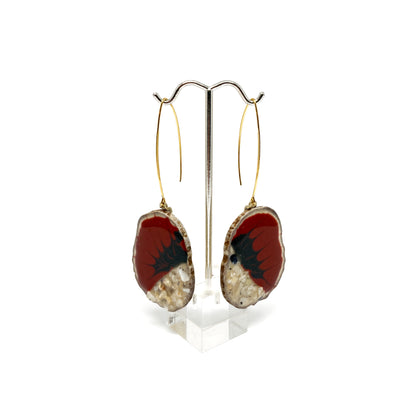 Two round earrings with red and black bird-shaped designs, displayed on a silver earring stand.