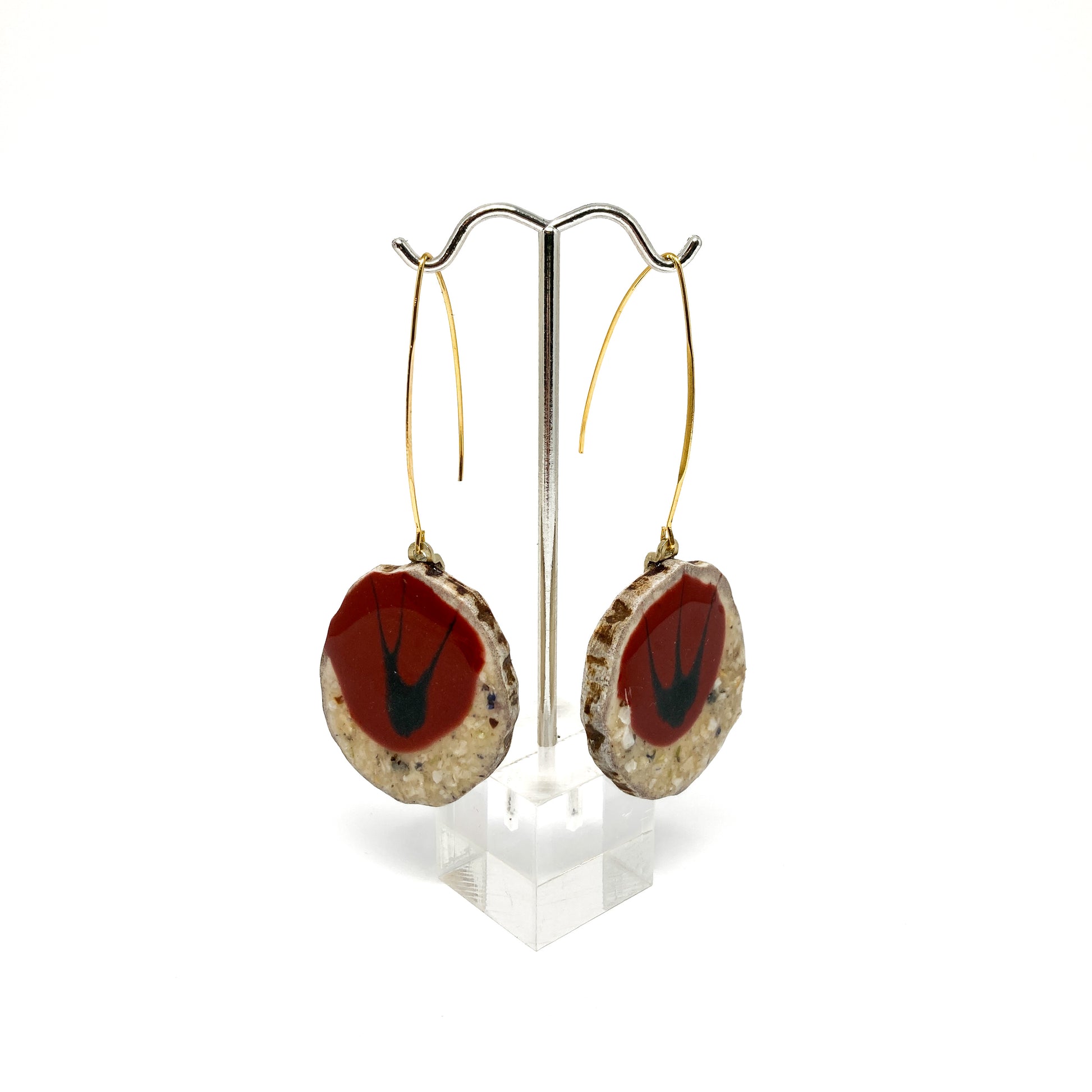 Two round earrings with red and black bird-shaped designs, displayed on a silver earring stand.