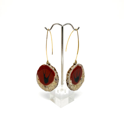 Two round earrings with red and black bird-shaped designs, displayed on a silver earring stand.