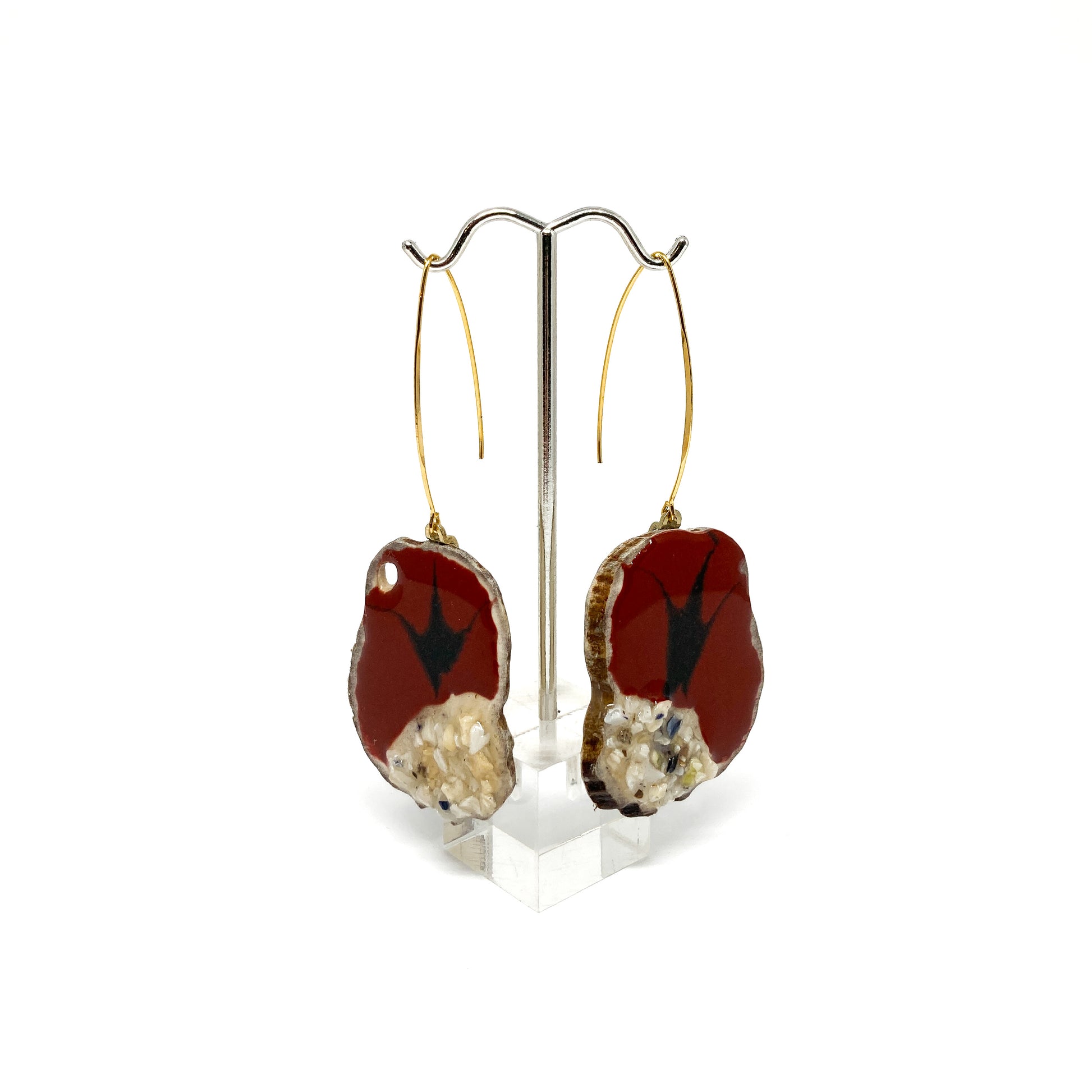 Two round earrings with red and black bird-shaped designs, displayed on a silver earring stand.