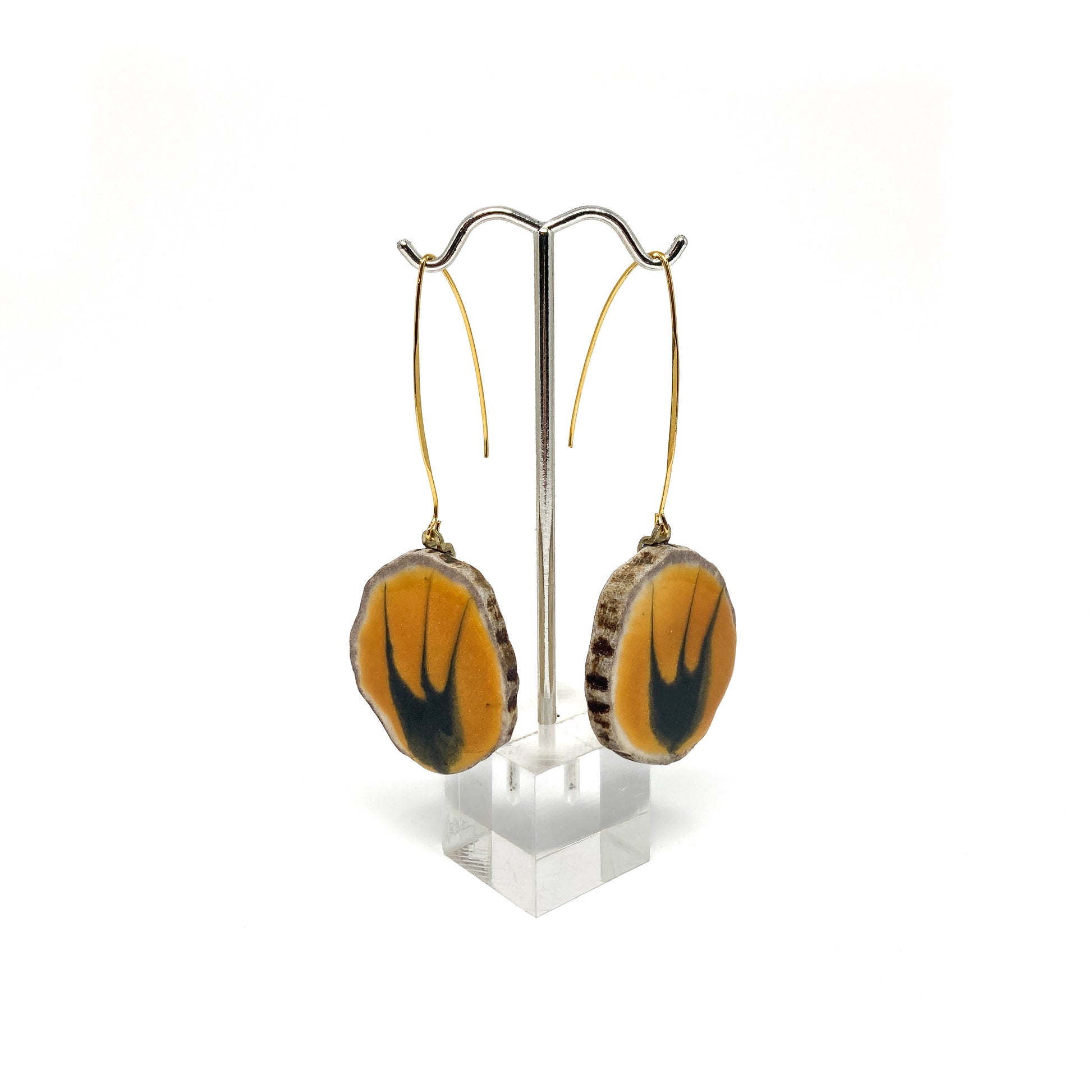 Two round earrings with yellow and black bird-shaped designs, displayed on a silver earring stand.