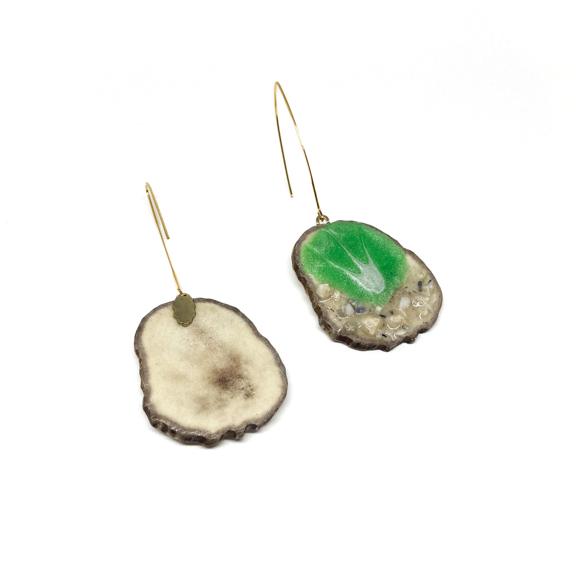 Two mismatched earrings, one with a green leaf-shaped design, the other with a slice of antler and a gold hook.