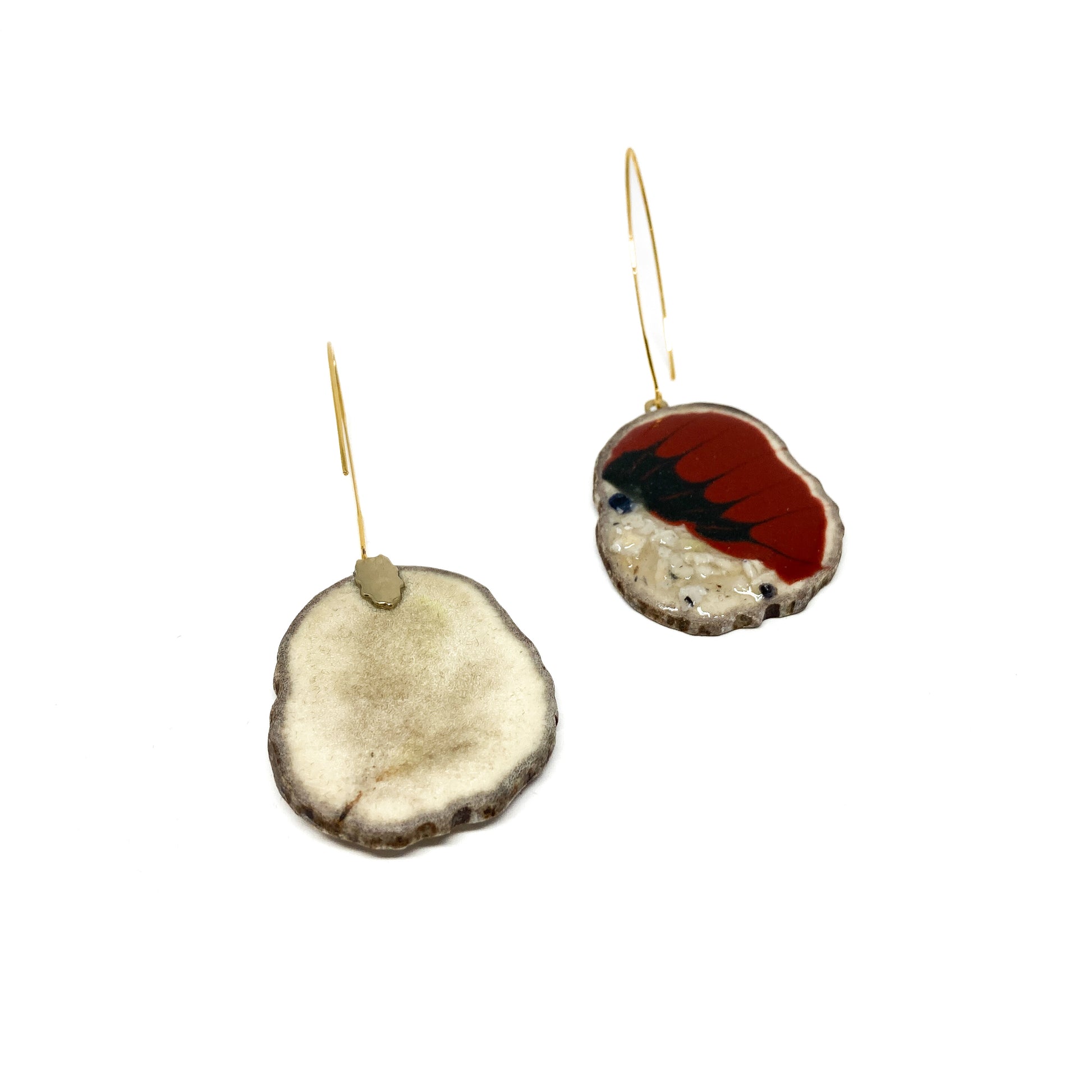 Two mismatched earrings, one with a red and black bird-shaped design, the other with a slice of antler and a gold hook.