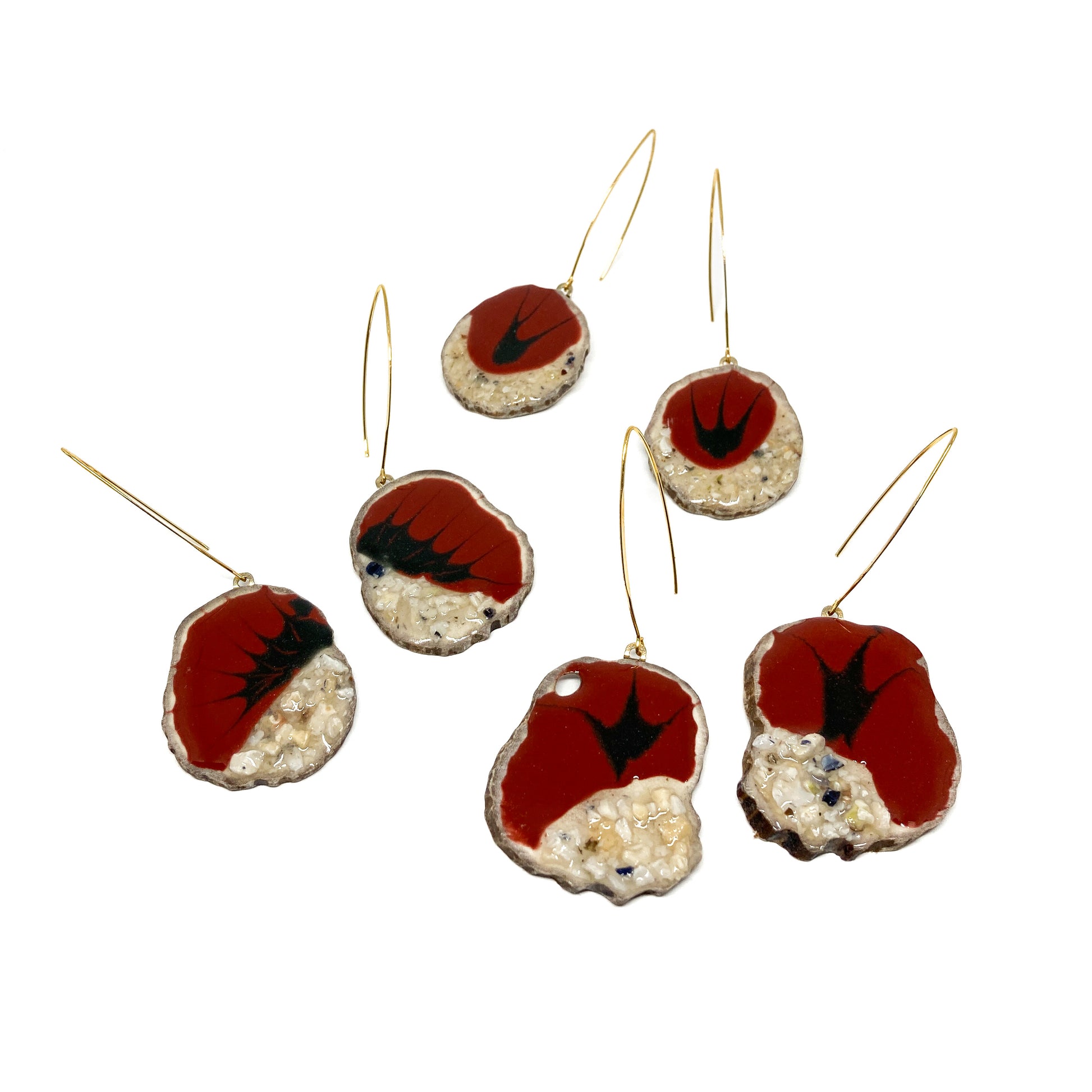 Two mismatched earrings, one with a red and black bird-shaped design, the other with a slice of antler and a gold hook.