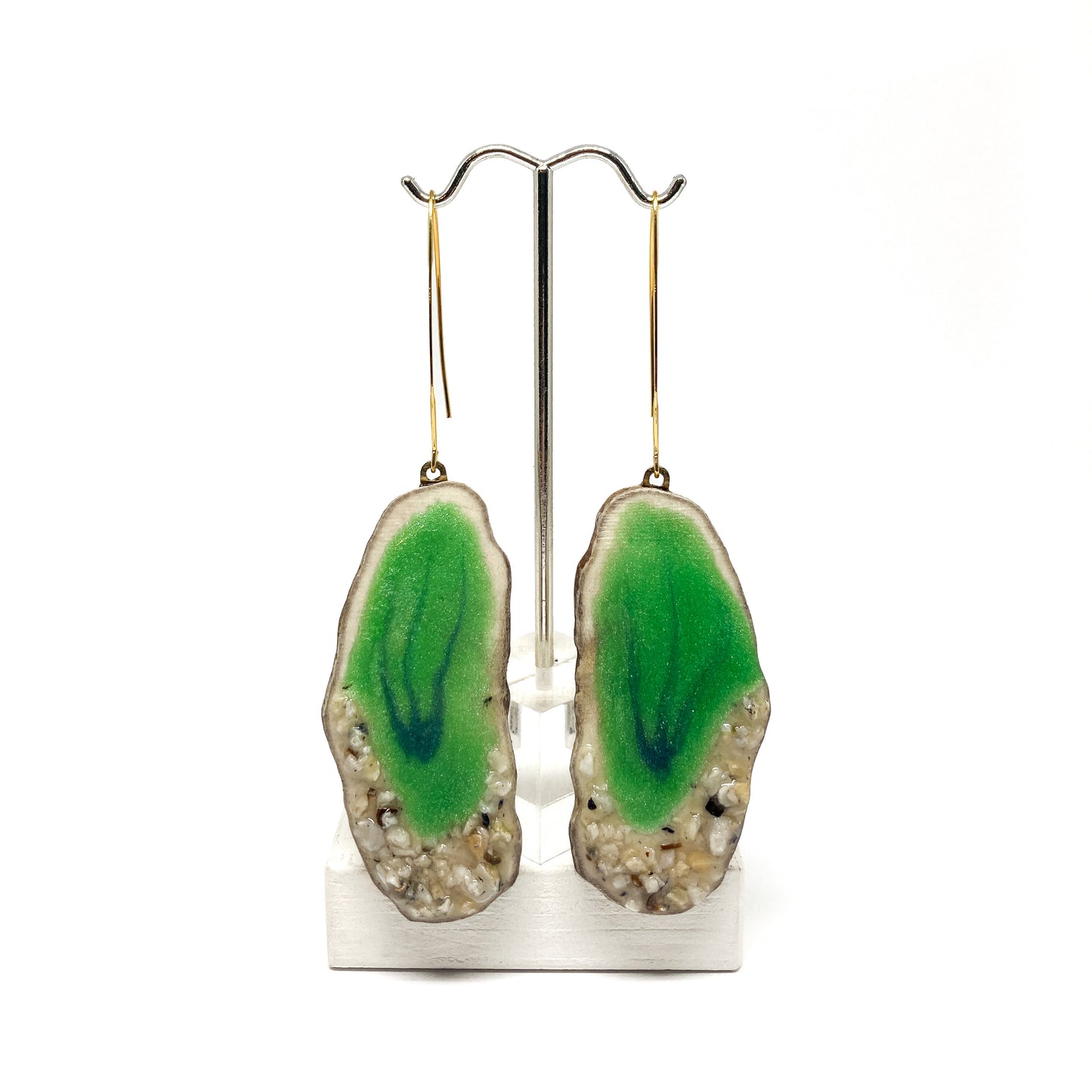Two round earrings with green geode-like designs, displayed on a silver earring stand.
